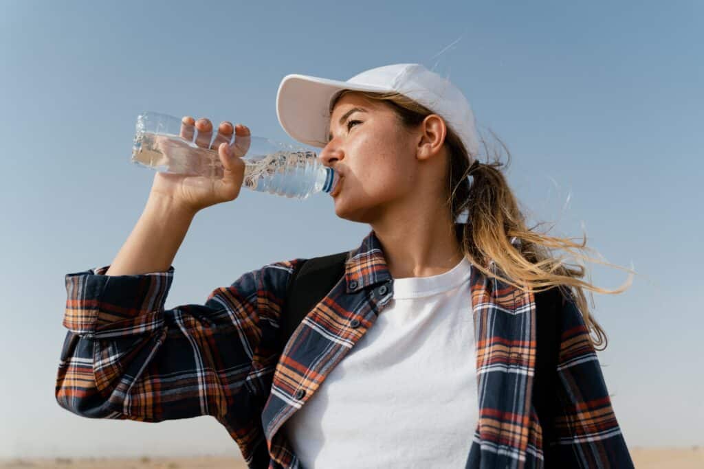 A woman outside staying hydrated by drinking from a water bottle.